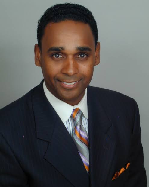 Archival studio portrait of Dwayne Ballen in a dark pinstripe suit from his network broadcast years