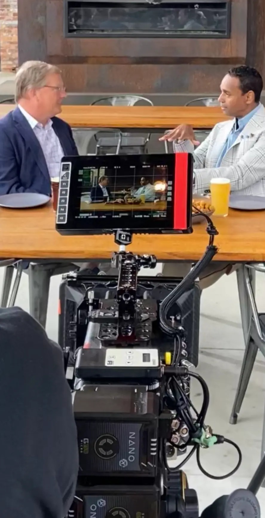 A two-person interview at a table filmed through a director's monitor showing the live shot