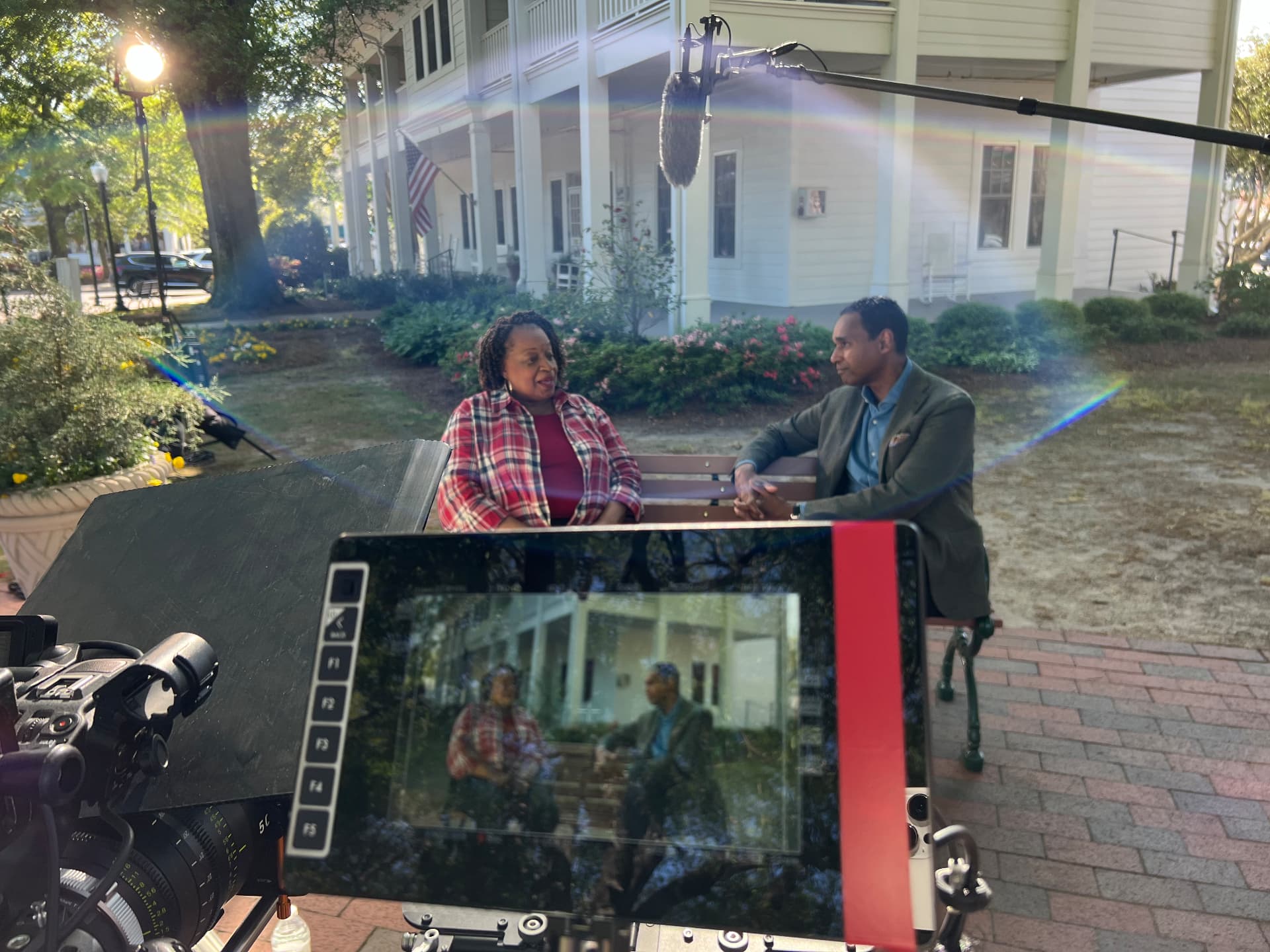 Dwayne Ballen conducting an on-location interview framed through a director's monitor, with a boom microphone and cinema camera on set