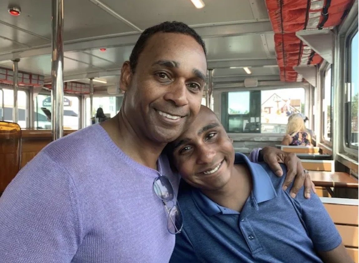 Dwayne Ballen with his arm around his son Julian, both smiling, aboard a boat