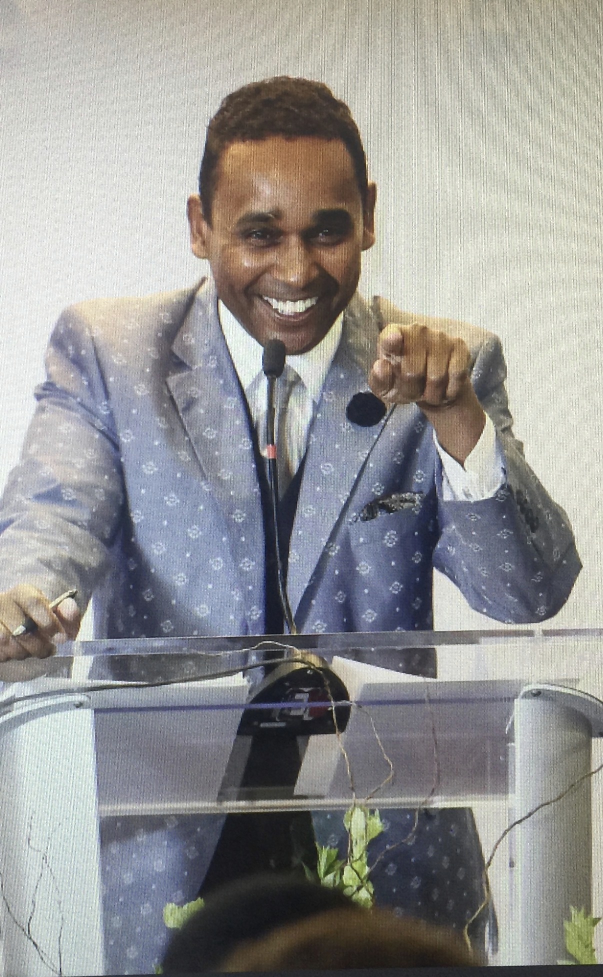 Dwayne Ballen smiling and addressing an audience from a transparent podium