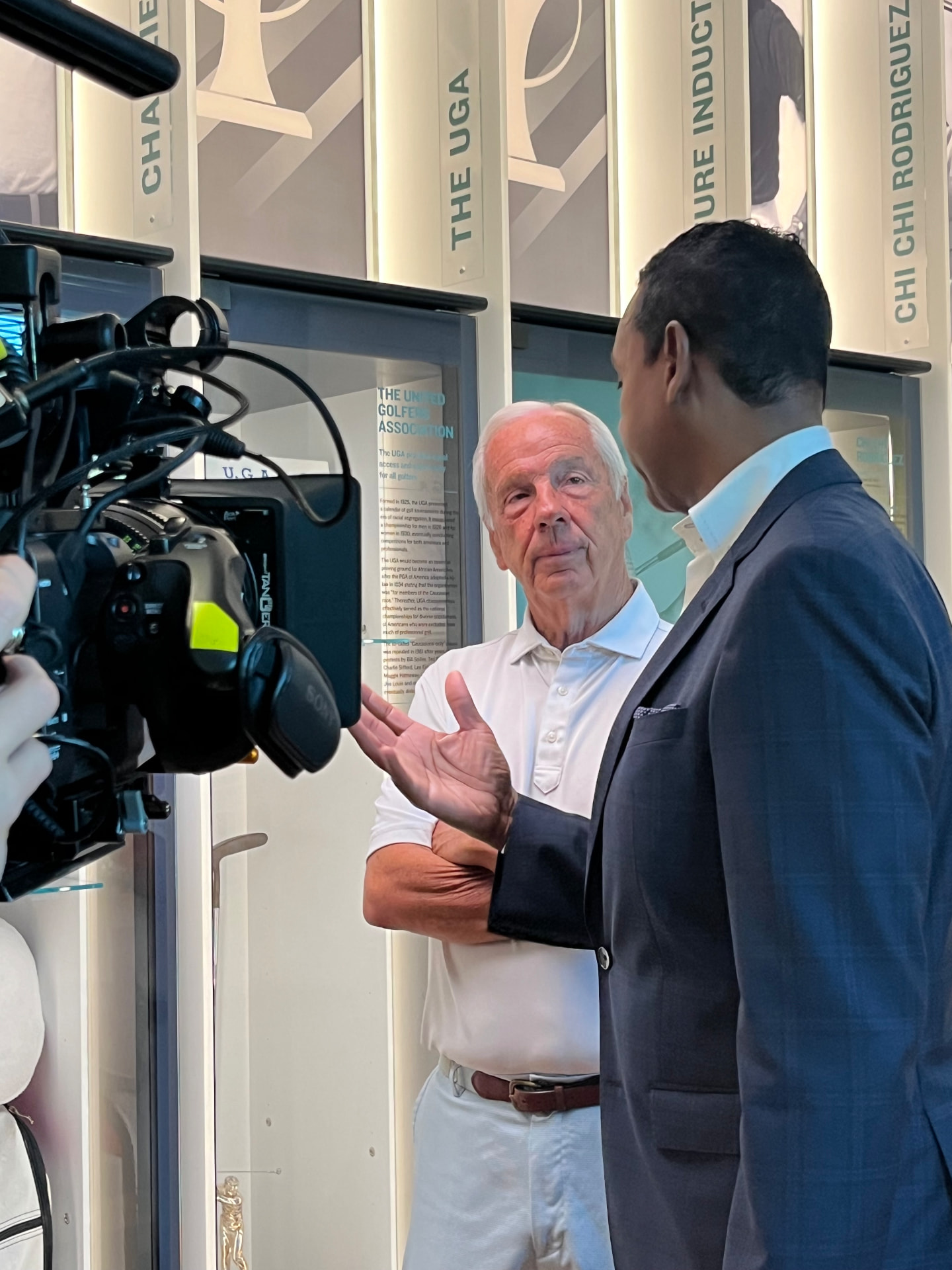Dwayne Ballen interviewing a subject on camera in front of a golf history museum exhibit