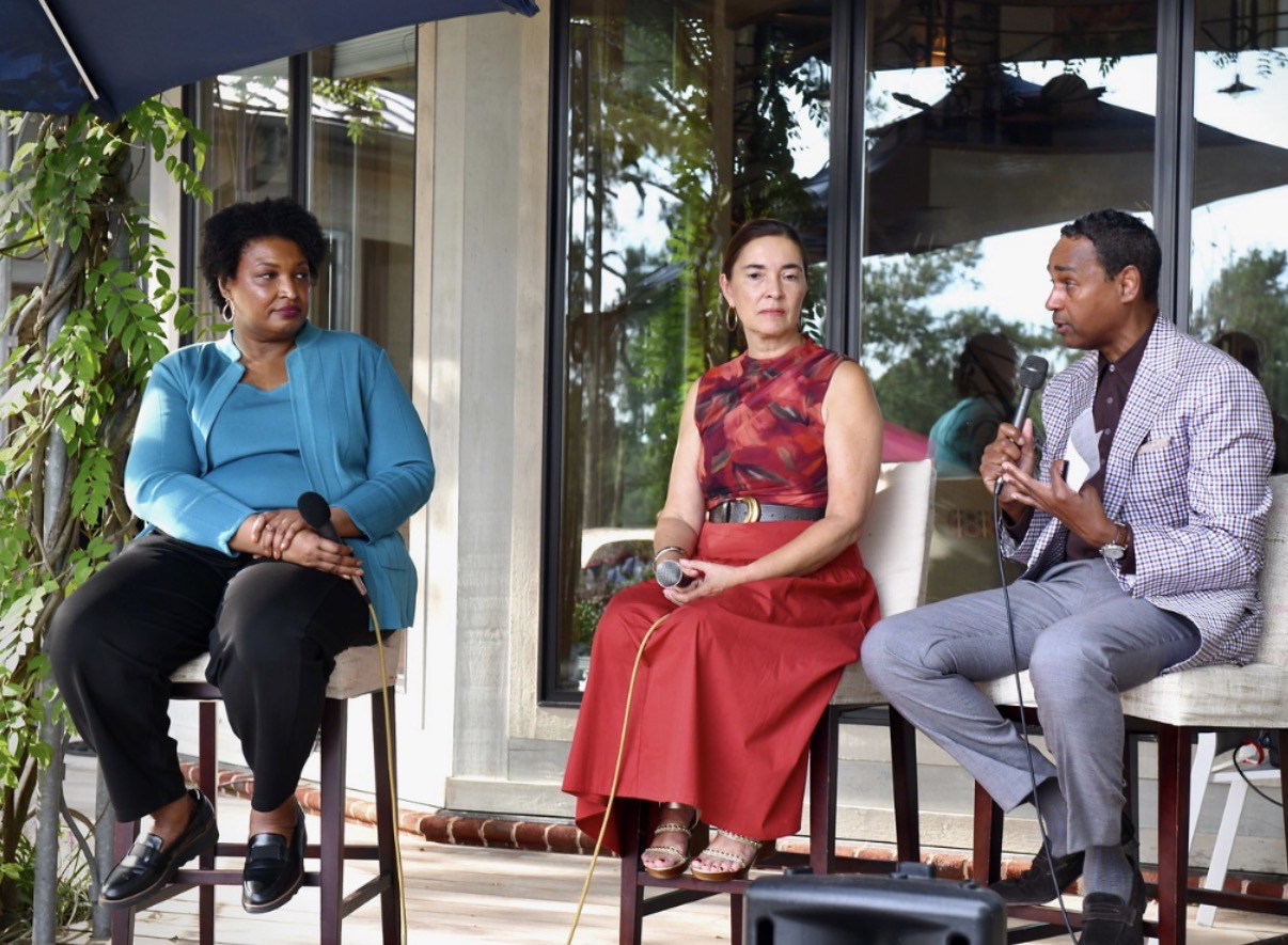 Dwayne Ballen holding a microphone while moderating an outdoor panel with two seated guests