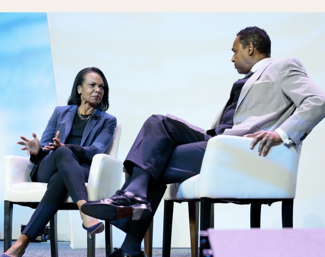 Dwayne Ballen and Condoleezza Rice in conversation on a conference main stage, seated in white chairs