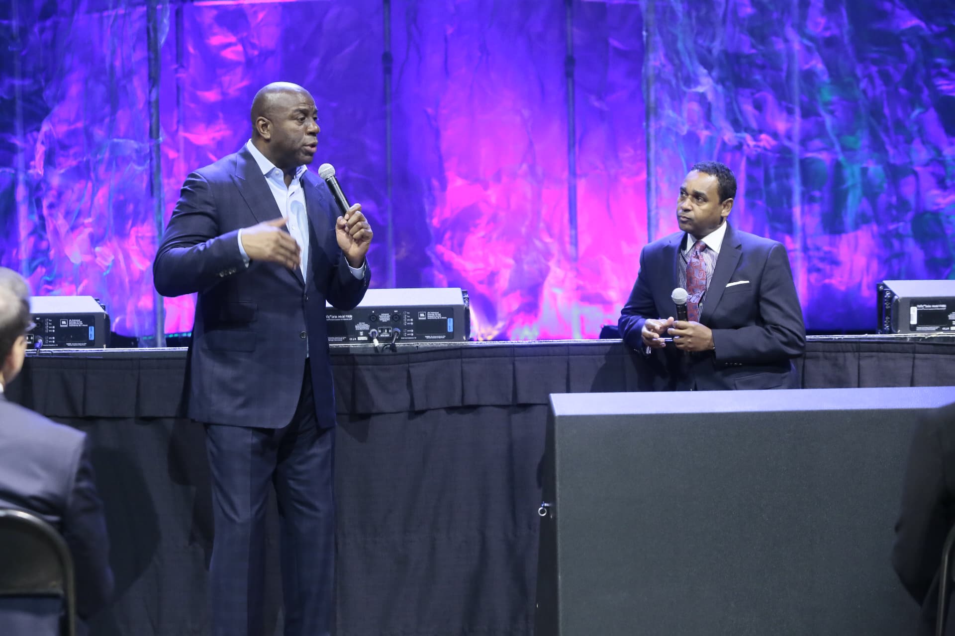 Dwayne Ballen holding a microphone on stage as Magic Johnson speaks during a live keynote conversation