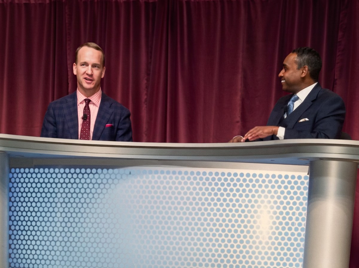 Dwayne Ballen in a one-on-one keynote conversation with Peyton Manning on a stage set with deep red curtains